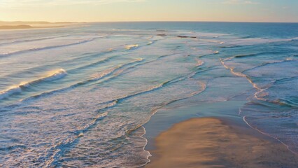 Sunlit beach at sunset with gentle waves rolling in.