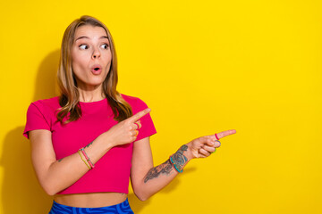 Surprised young woman pointing enthusiastically to the side against a vibrant yellow background in...