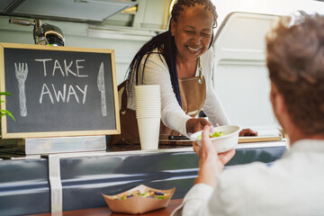 African american senior woman serving takeaway food inside food truck - Small business and summer concept - Soft focus on female face