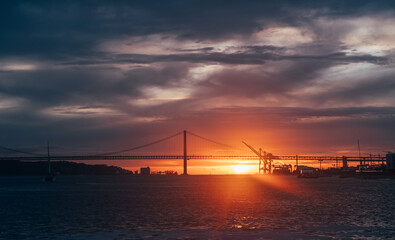 Picturesque sunset moment image of "25 de Abril Bridge" and city port cranes in Lisbon late March.