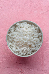White rice, cooked. A bowl of boiled long grain rice, a simple side dish, on a pink background, shot from above with a place for text