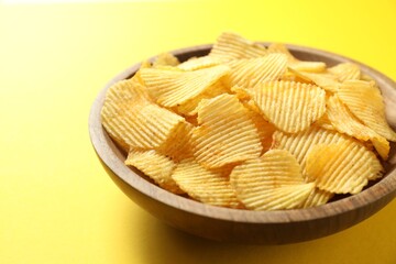 Tasty potato chips in bowl on yellow background, closeup