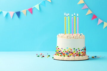 Delicious bento cake with colorful sprinkles and burning candles on light blue table. Space for text