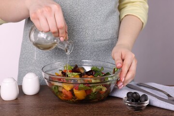 Woman pouring apple vinegar onto tasty salad at wooden table against grey background, closeup