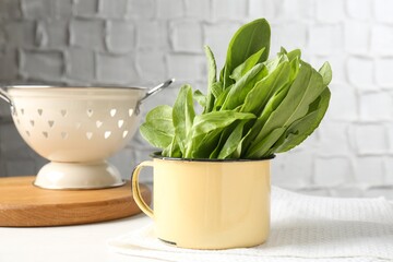 Fresh sorrel leaves in bowl and colander on white table