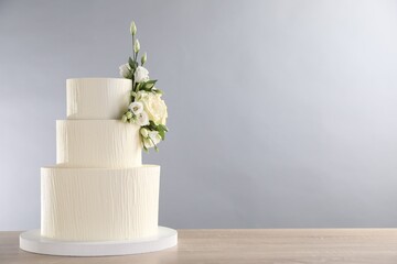 Delicious wedding cake decorated with flowers on wooden table against grey background. Space for text