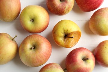 Rotten apple among fresh ones on white wooden table, flat lay