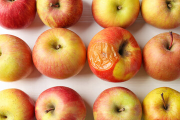Rotten apple among fresh ones on white wooden table, flat lay