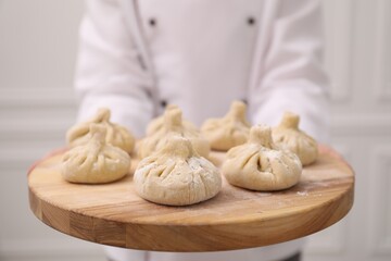Chef holding board with uncooked khinkali indoors, closeup