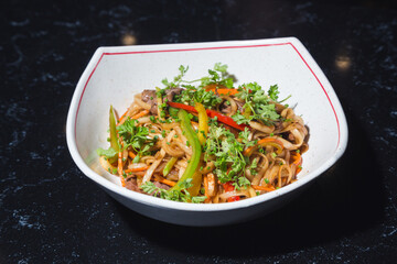Buckwheat wok noodles with vegetables in a white plate on a dark table