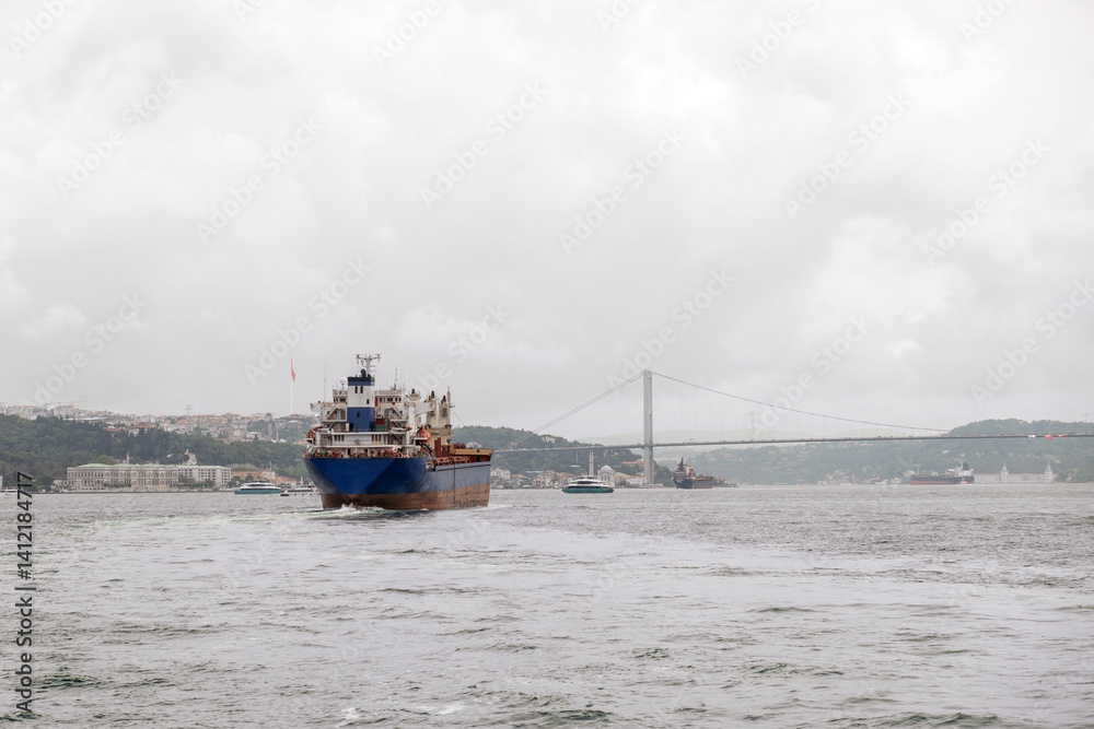 Aufkleber bosphorus strait with a cargo ship navigating under an iconic bridge on an overcast day in istanbul,