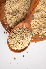 Peeled hemp seeds in wooden spoon and on plate on light background, top view. Superfood, healthy tasty organic hemp seeds, source of omega 3 fatty acids, protein. Supplement to healthy diet