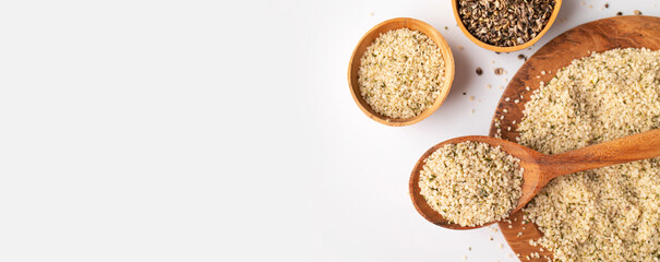 Peeled hemp seeds in wooden spoon and on plate on light background, top view. Superfood, healthy tasty organic hemp seeds, source of omega 3 fatty acids, protein. Supplement to healthy diet