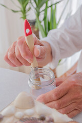 Senior person dipping brush in varnish to coat seashell jewelry box