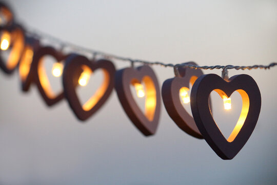Close-up of a row of Heart shaped illuminated string lights hanging in front of a grey background
