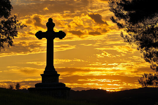 Stone cross silhouette at sunset with dramatic orange sky and peaceful landscape - Powered by Adobe