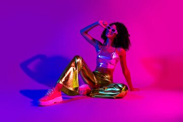Stylish young woman in shiny outfit with neon lighting, expressing vibrant energy and modern glamour