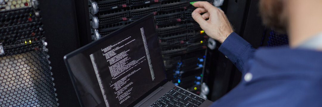 Website header shot of technician working with laptop connected to computer server, managing server rack with detailed interface and various indicator lights in background