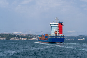 Container ship navigating the Bosphorus Strait, showcasing vibrant blue and red colors against the...