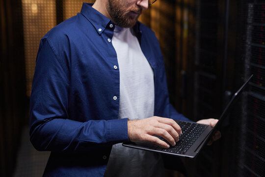 Man focusing on his laptop in a data center, surrounded by server racks, concentrating on his task in technology-driven environment