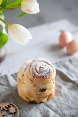 Easter Bread or Kulich with raisins. Easter yeast twisted cake Cruffin, painted eggs and tulip flowers on a stone background. Easter food.