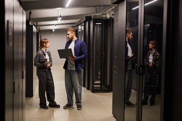 Two IT professionals discussing data management in a modern server room with servers visible...