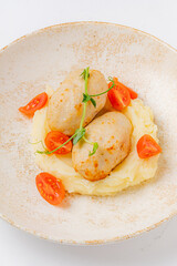 Savory dumplings rest atop smooth mashed potatoes, adorned with vibrant tomato slices
