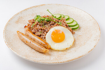 A hearty breakfast features buckwheat, sausages, a sunny-side-up egg, and fresh cucumbers
