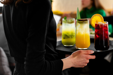 A close-up of a server holding a black tray with three colorful cocktails, featuring vibrant...