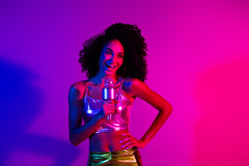 Naklejka premium Vibrant portrait of a young woman singing with a microphone against neon pink and purple lights, embracing a trendy and glowing atmosphere.