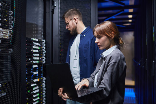 IT professionals in a data center managing server operations while collaborating on tasks with laptops. Focused on server health and data management
