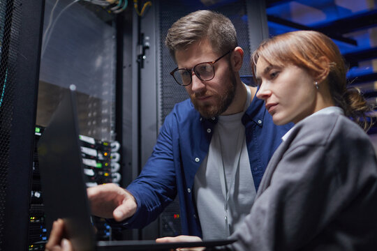 Multiracial team working on server maintenance in a data center. Man and woman collaborating while examining server rack and discussing technical details
