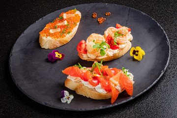 Three delightful seafood canapés arranged artfully on a dark slate plate, garnished with flowers