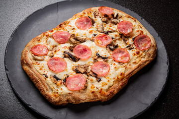 Freshly baked pizza featuring pepperoni slices and mushrooms resting on a textured black surface