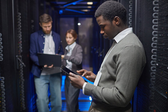 Team of IT professionals working with gadgets in server room analyzing data on devices. Focus on technology and collaboration in high-tech environment - Powered by Adobe