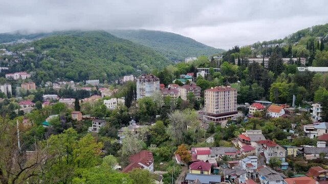 Mountainous cityscape in Sochi, residential buildings blending with verdant forest backdrop under overcast spring skies