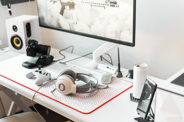 Well-organized gaming and creative workspace in bright tones features large monitor, white keyboard, gaming mouse on soft pad, and professional headphones. Energy drink add to setup work and play.