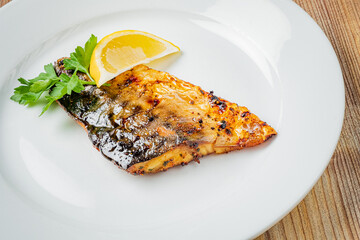 A grilled fish fillet sits elegantly on a white plate, garnished with lemon and parsley