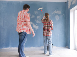 Happy couple renovating new house apartment priming wall before painting . Family man woman repair flat themselves.