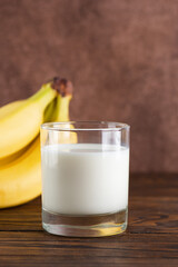 Banana milk in a glass with bananas on a wooden table. Traditional Korean drink. Vertical orientation.