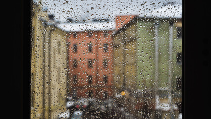 Raindrops sliding on window glass blurring buildings in the background