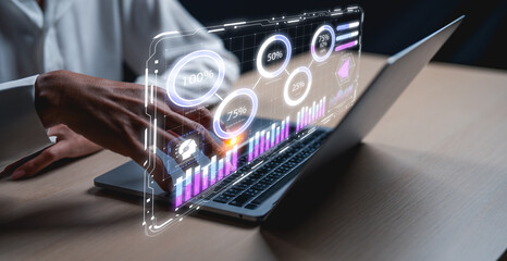 Fototapeta premium A hand interacts with a futuristic display of graphs and data hovering above a laptop, illustrating technology and data analysis.