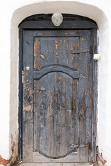 An old wooden door in a dilapidated condition with rust, peeling paint and an antique design. It appears to be part of an abandoned building with an arched doorway.