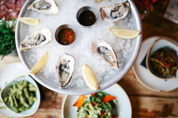 A detailed close-up of a chilled oyster platter on a bed of crushed ice, garnished with lemon wedges and accompanied by dipping sauces, set in a rustic seafood restaurant with selective focus