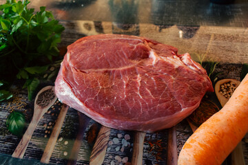 Raw beaf steak with carrot and parsley on cutting board. Raw meat, herbs and vegetable on table. Kitchen interior. Steak preparation process. Food styling. Marble steak on cutting board.