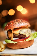 Juicy cheeseburger with melted cheddar, lettuce, and tomato on a toasted bun in warm bokeh restaurant lighting, soft focus.
