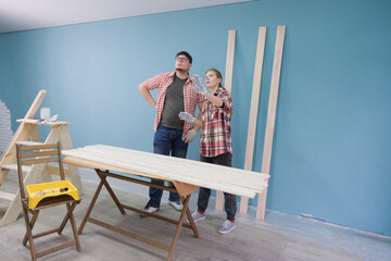 Happy couple renovating new house apartment painting wood boards together. Family man woman repair flat themselves.