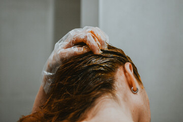 Naklejka premium A woman applies hair dye with a special brush wearing gloves at home in the bathroom