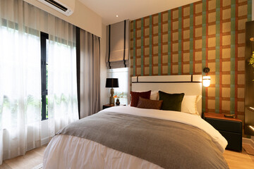 stylish bedroom interior design with wallpaper and black patterned pillows on bed and decorative table lamp.