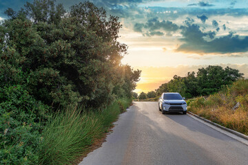 A modern car is parked along a peaceful forest road under a glowing sunset sky, capturing the essence of a tranquil countryside journey.